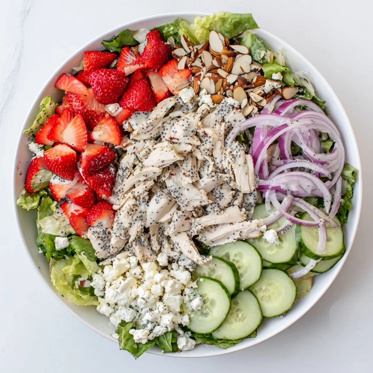 A colorful bowl of Strawberry Poppy Seed Chicken Salad with juicy red strawberries, greens, and shredded chicken, perfect for a light summer lunch.