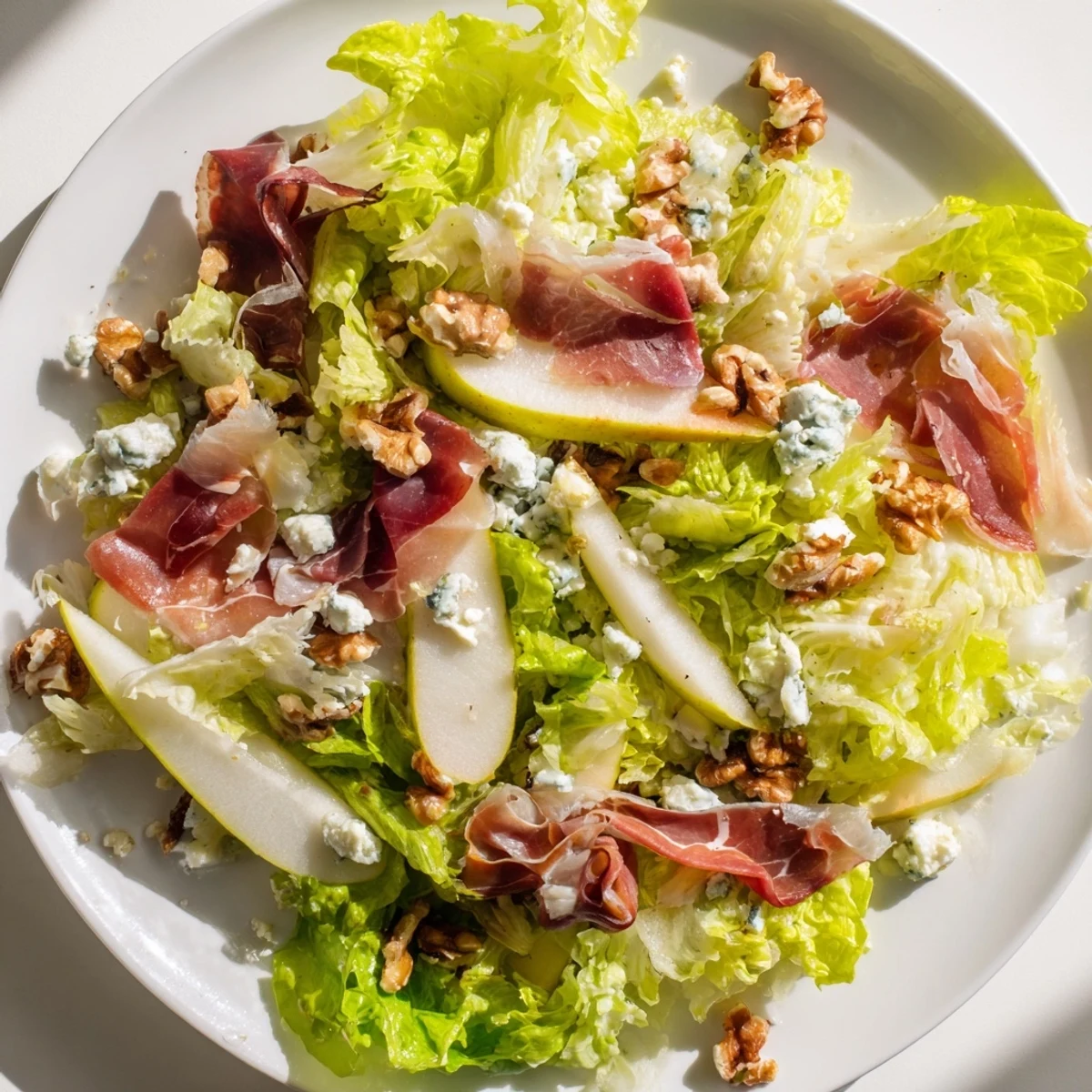 A close-up of pear wedges, creamy blue cheese, and crispy prosciutto on frisée leaves, ready for a light lunch.