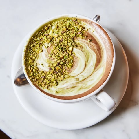 Creamy pistachio milk latte topped with crushed nuts, a delightful coffeehouse indulgence.  