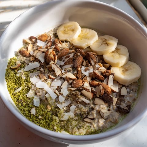 Creamy High-Protein Eggnog Matcha Overnight Oats with banana slices and toasted coconut, ready to eat.