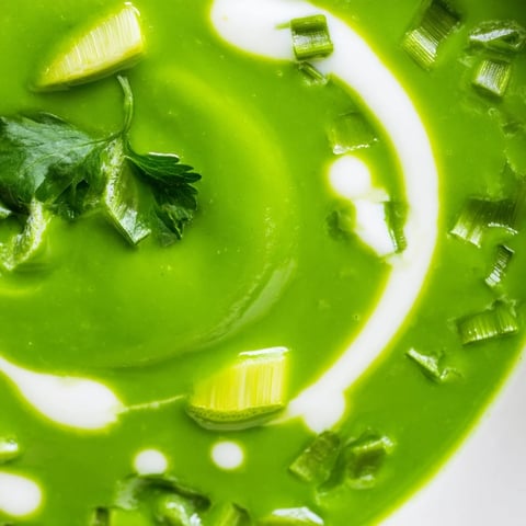 Creamy Spinach Coriander Lemongrass Soup served in a white bowl, garnished with cilantro leaves and lime wedges.  