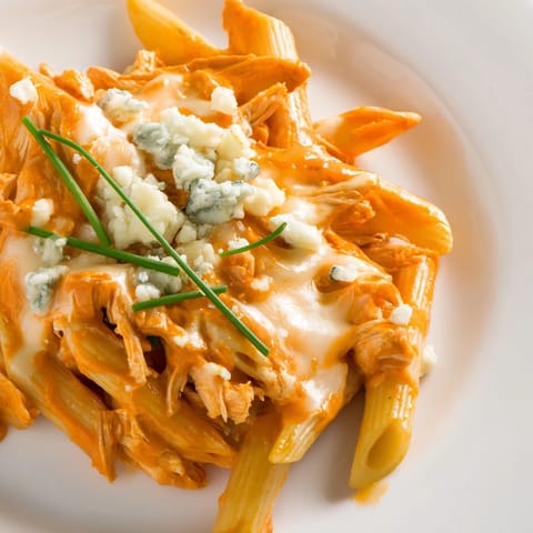 Creamy Buffalo Chicken Pasta with shredded chicken and penne noodles, served beside a cold beer and celery.  