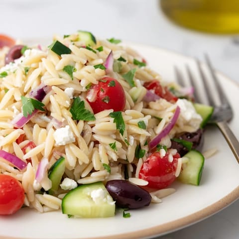 This refreshing Greek Orzo Salad is perfect for picnics, featuring colorful vegetables and briny feta cheese.