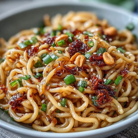 Spicy Chili Crisp Noodles with Garlic and Scallions in a steaming bowl, garnished with roasted peanuts and fresh green onions for bold flavor.