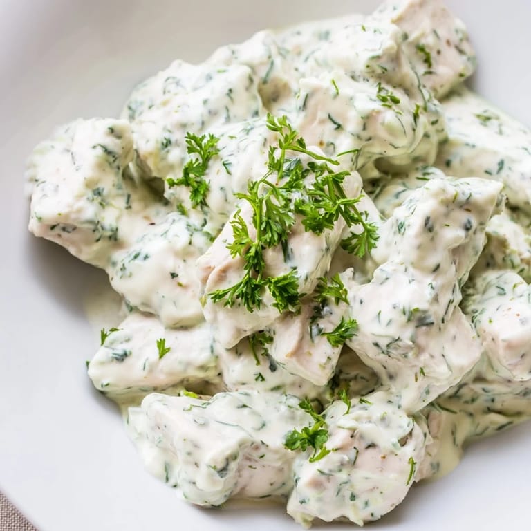 Tender Green Goddess Chicken Salad on a bed of crisp greens, drizzled with vibrant herb dressing and garnished with bright red tomatoes.