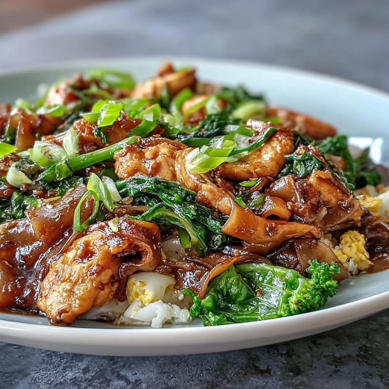 A plated serving of Authentic Thai Pad See Ew, garnished with lime wedges and savory chicken stir-fried with flat noodles.